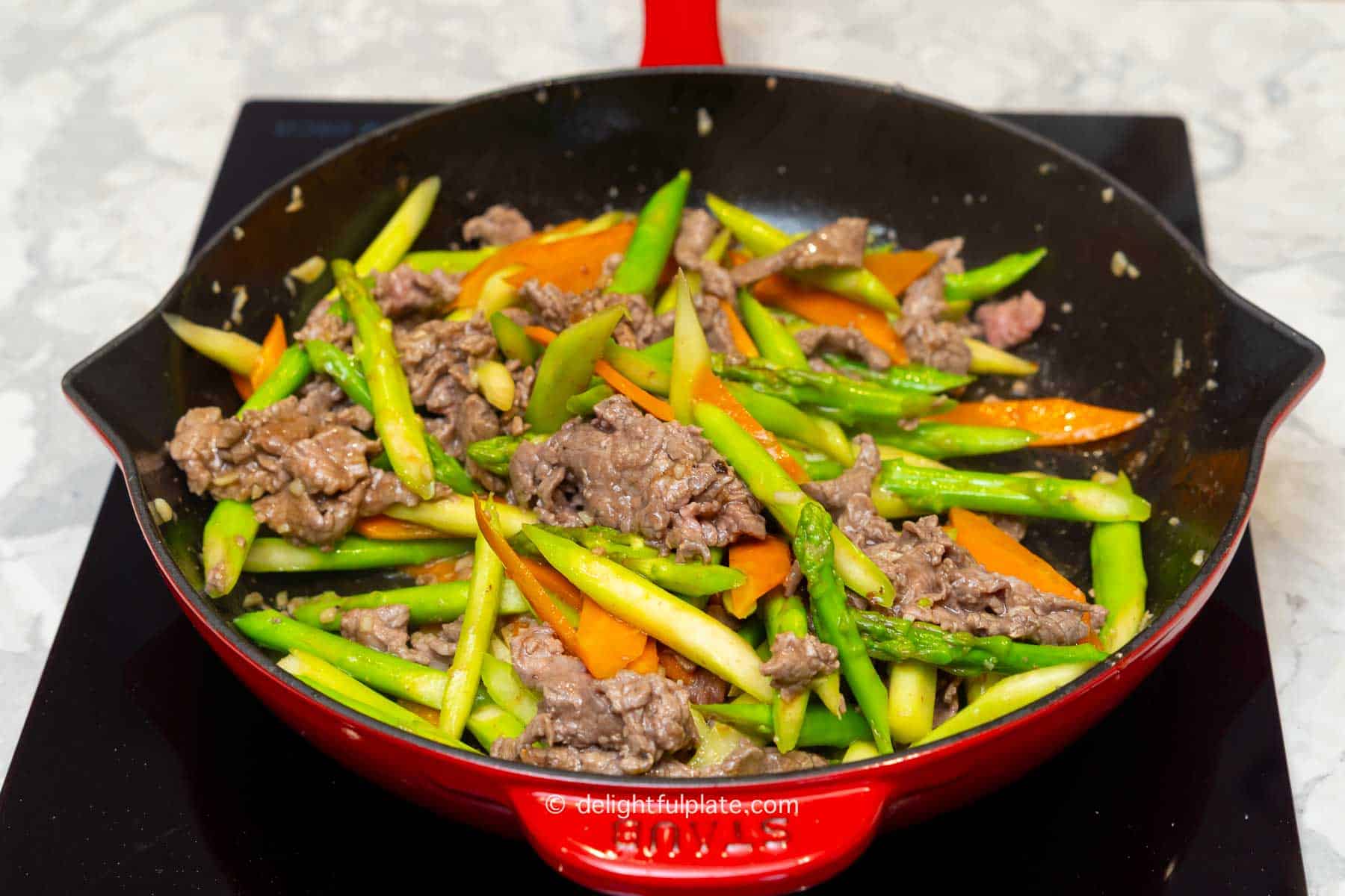 beef, asparagus and carrot being stir-fried together in the pan.