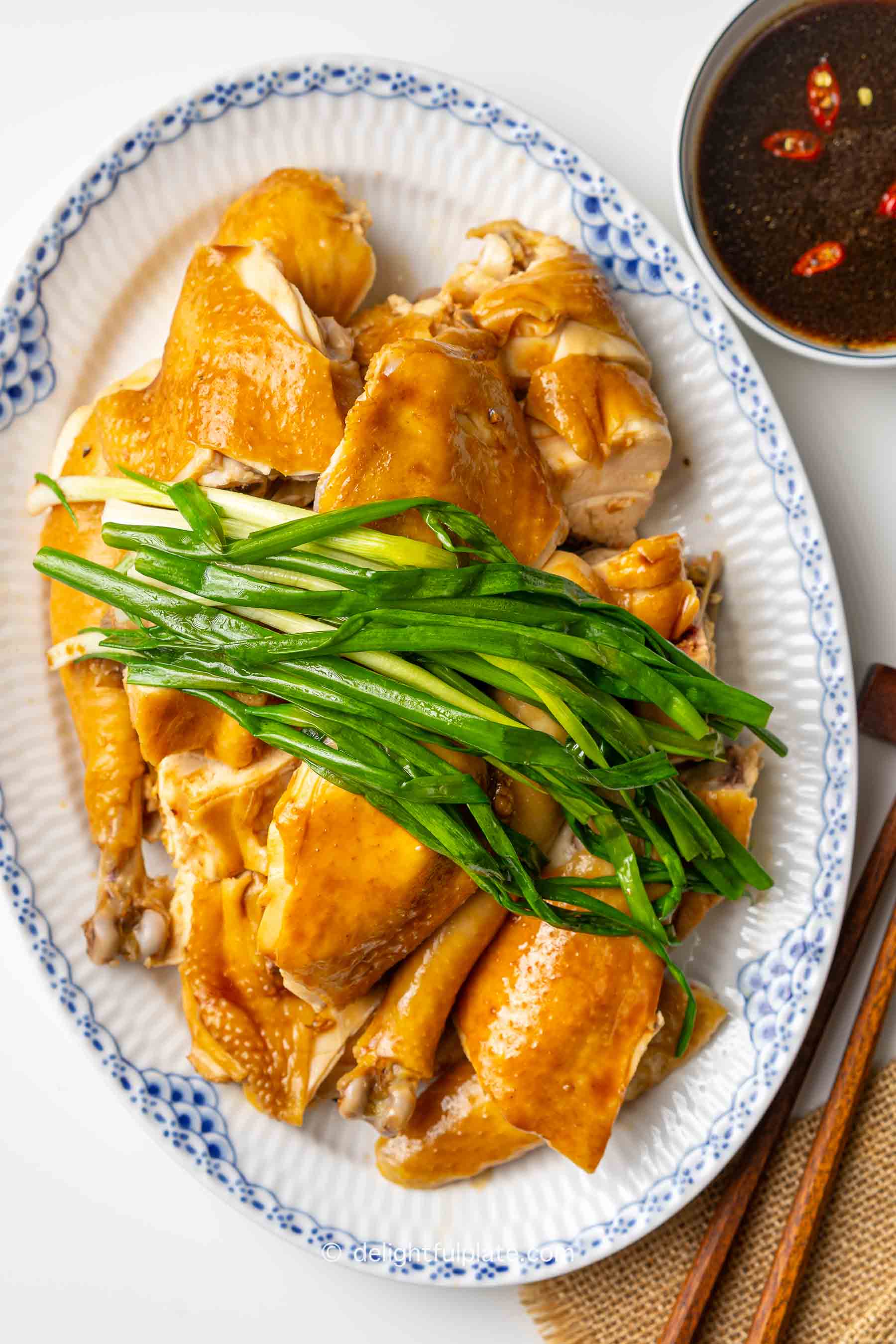 a plate of Vietnamese steamed chicken with fish sauce, scallion greens (Ga hap mam nhi) and a bowl of dipping sauce.