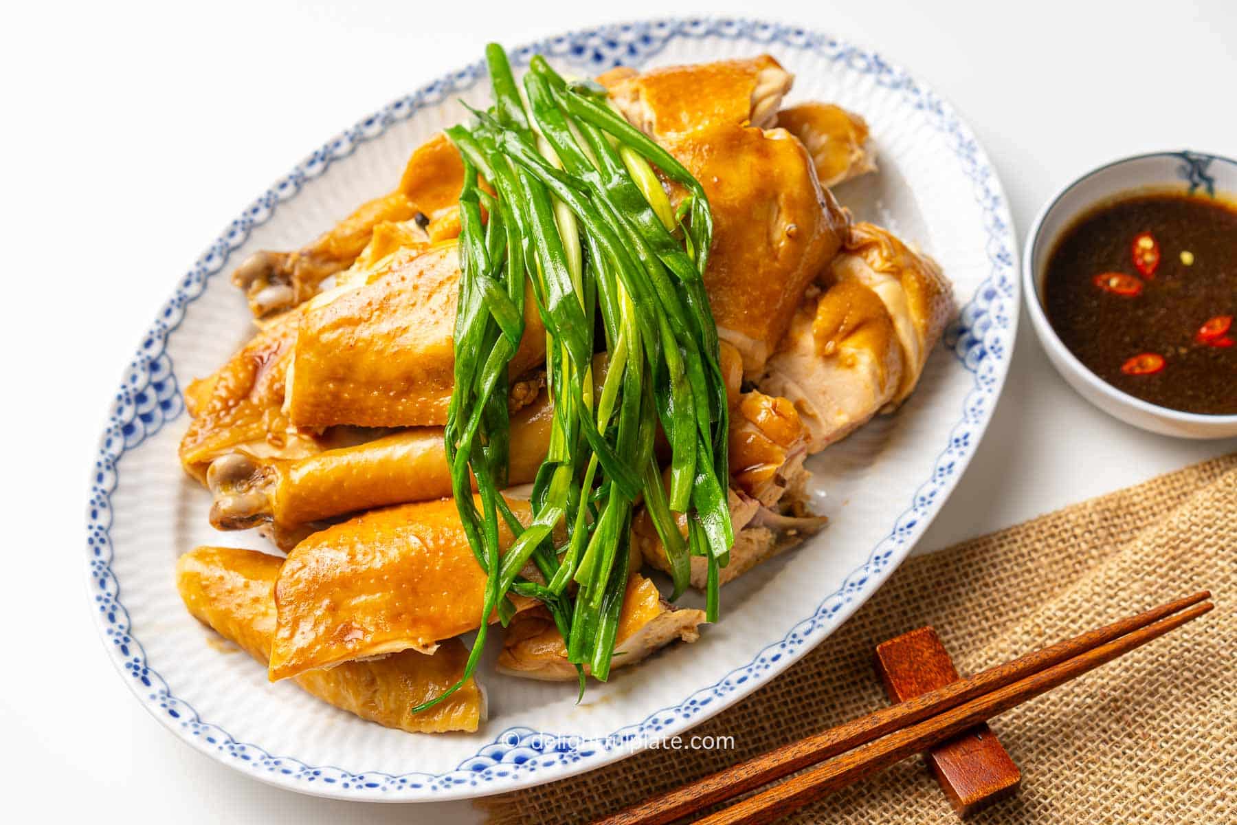 a plate of Vietnamese steamed chicken with fish sauce, scallion greens (Ga hap mam nhi) and a bowl of dipping sauce.