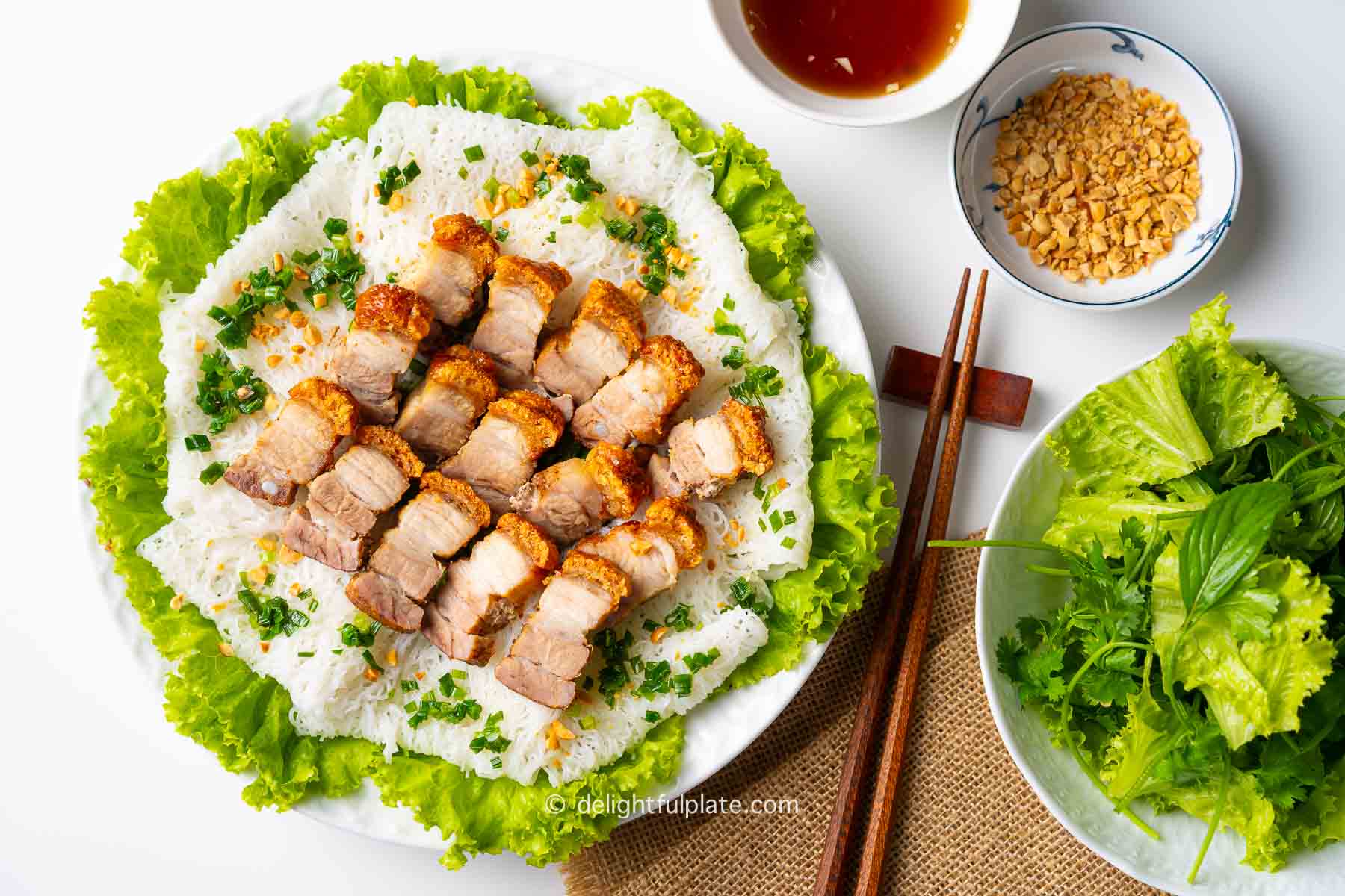 a plate of Vietnamese crispy roasted pork belly on a bed of vermicelli sheets, served with lettuce, herbs and dressing.