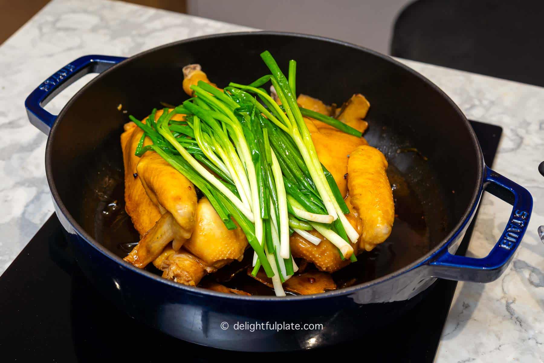 a deep pan containing steamed chicken, reduced sauce and cooked scallions.