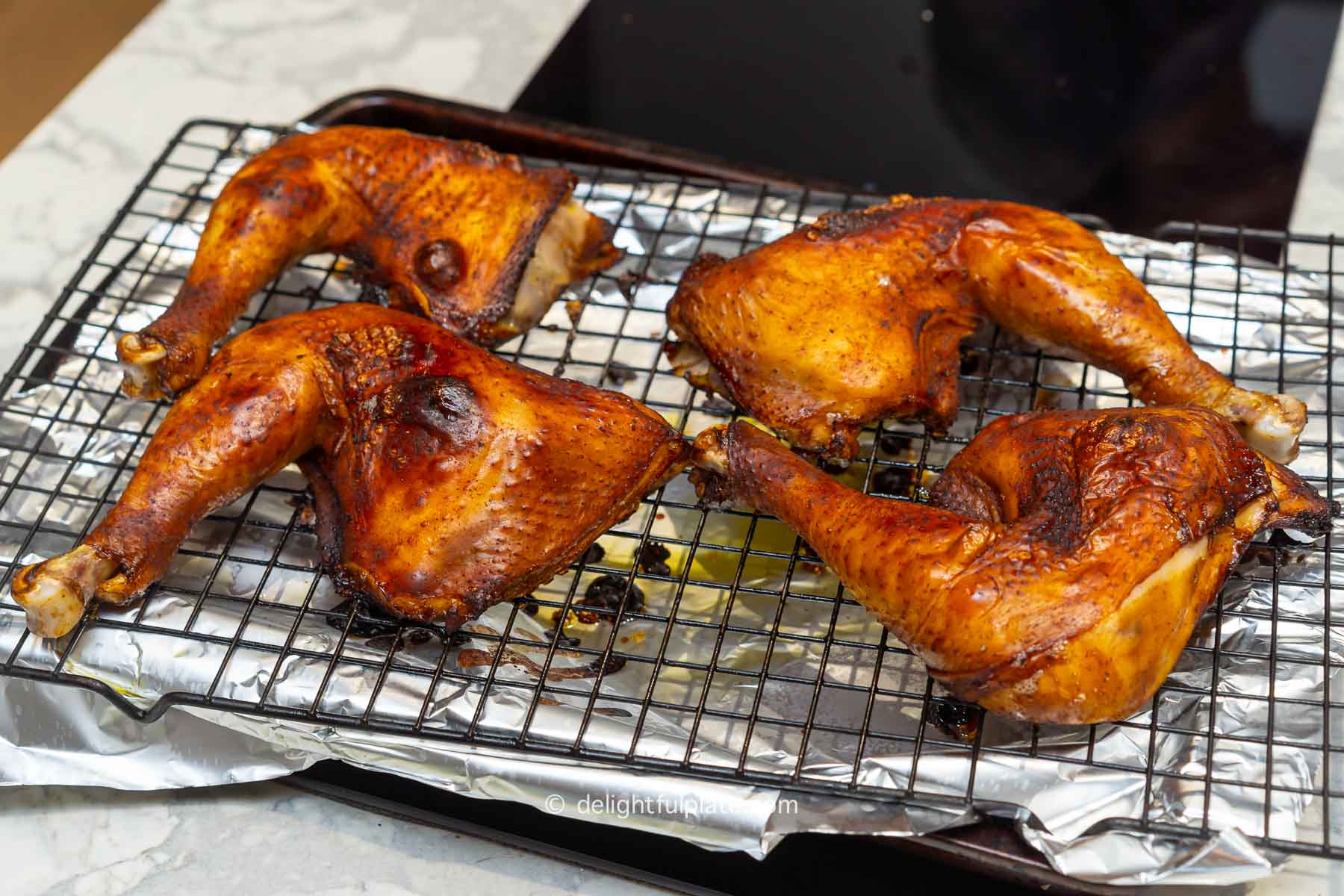 four roasted chicken legs with golden blistered skin on a wired rack.